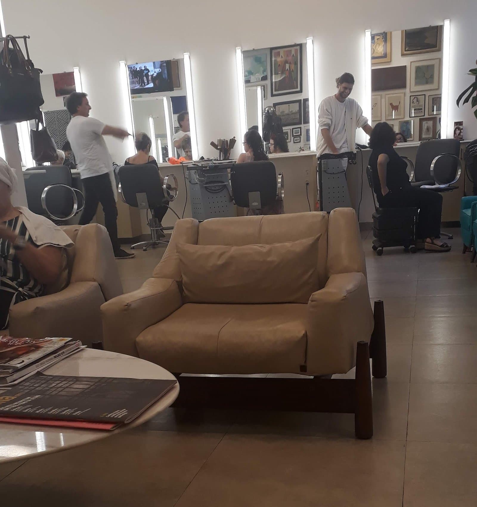 Poltrona de couro claro na espera, com as estações de corte e a parede de quadros ao fundo