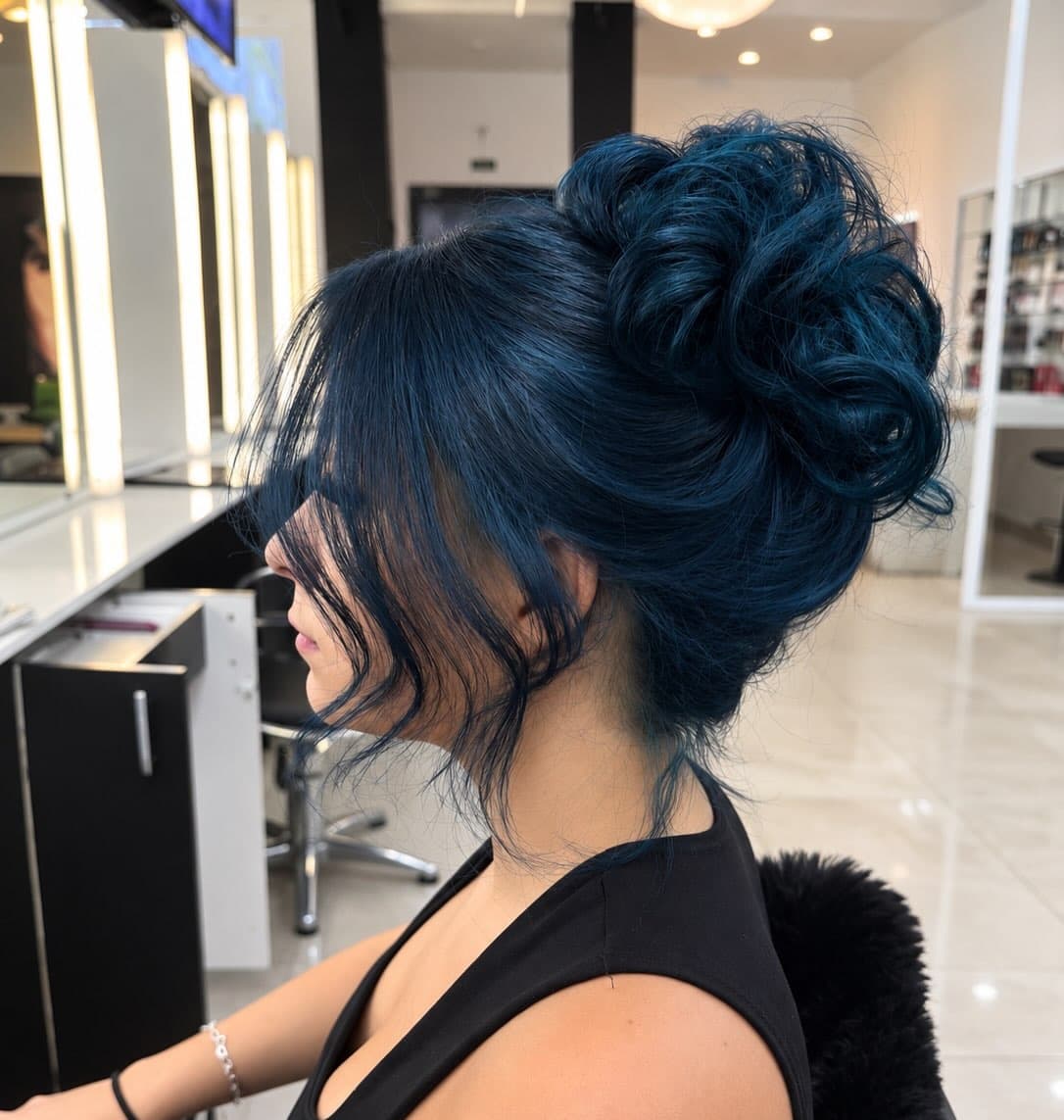 Cabelo tingido de azul escuro preso num coque alto, de perfil, na bancada do salão