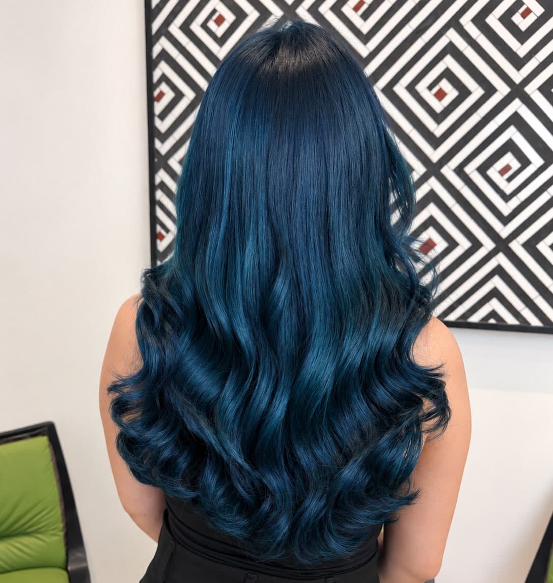 Cabelo longo tingido de azul escuro, com ondas, diante do quadro geométrico preto e branco do salão