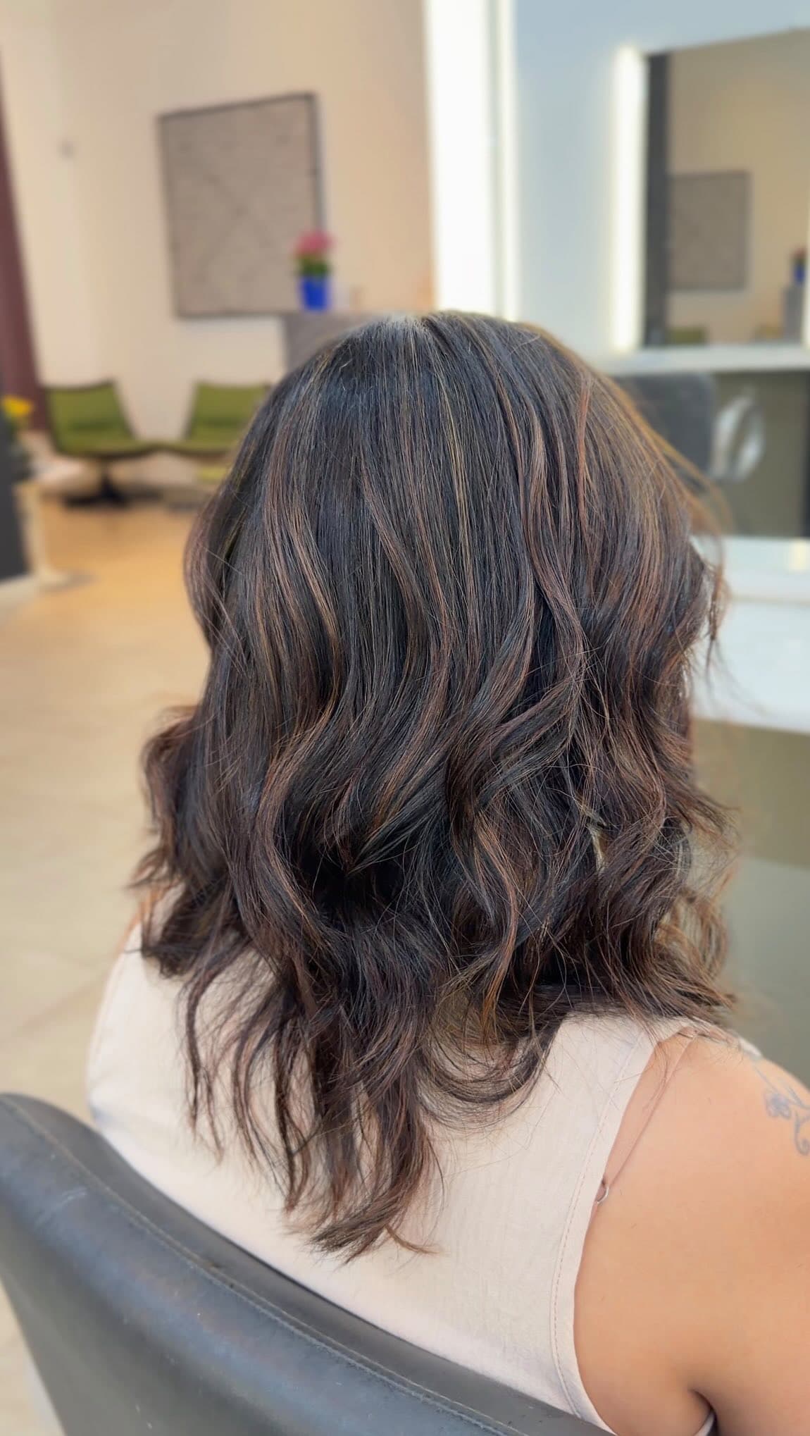 Cabelo castanho escuro com reflexos cobre e ondas, visto de costas na cadeira do salão