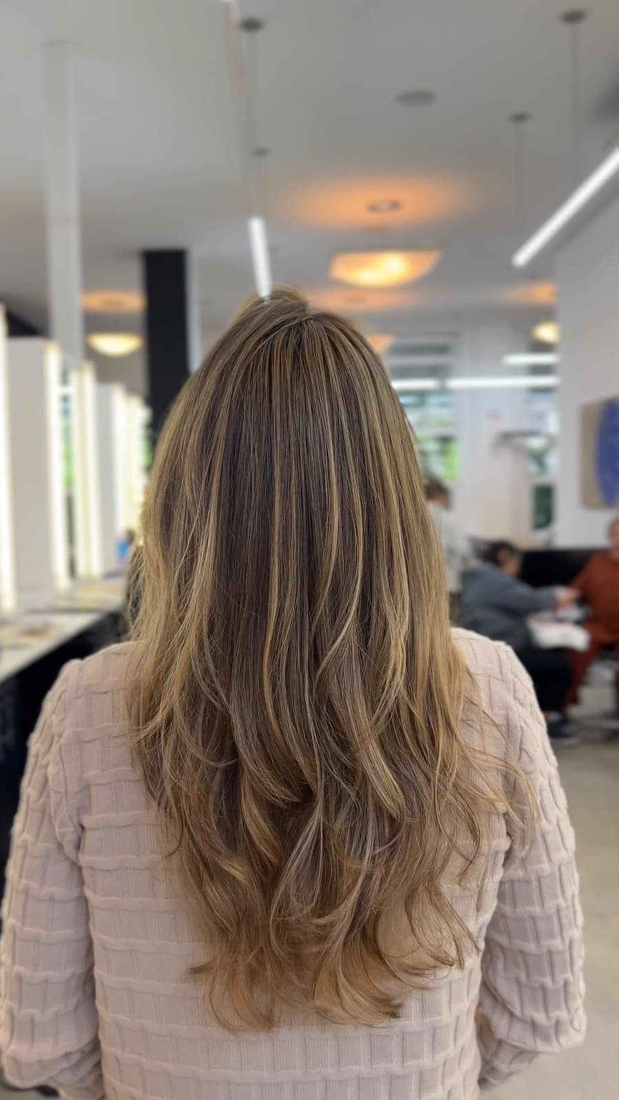 Cabelo longo em camadas, do castanho ao loiro iluminado, visto de costas no salão